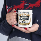 Person holding a mug with text 'We love and support Pastor Johnny and Janet for life' against a dark sweater background.